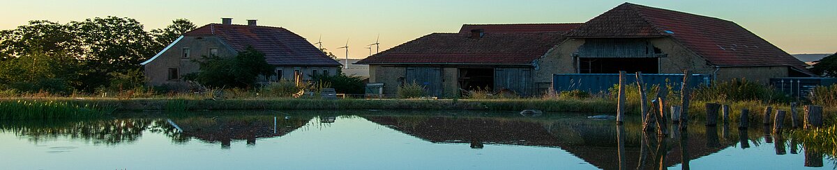 Humusland Hof Nordpfalz – Morgendämmerung Humusland Hof in der Nordpfalz – Hofgebäude spiegeln sich im Teich bei Morgendämmerung