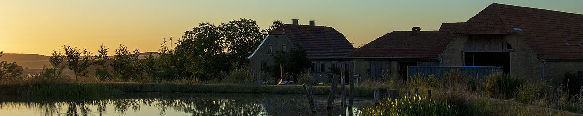Humusland Hof Nordpfalz – Abenddämmerung Humusland Hof in der Nordpfalz – Hofgebäude spiegeln sich im Teich bei Abenddämmerung