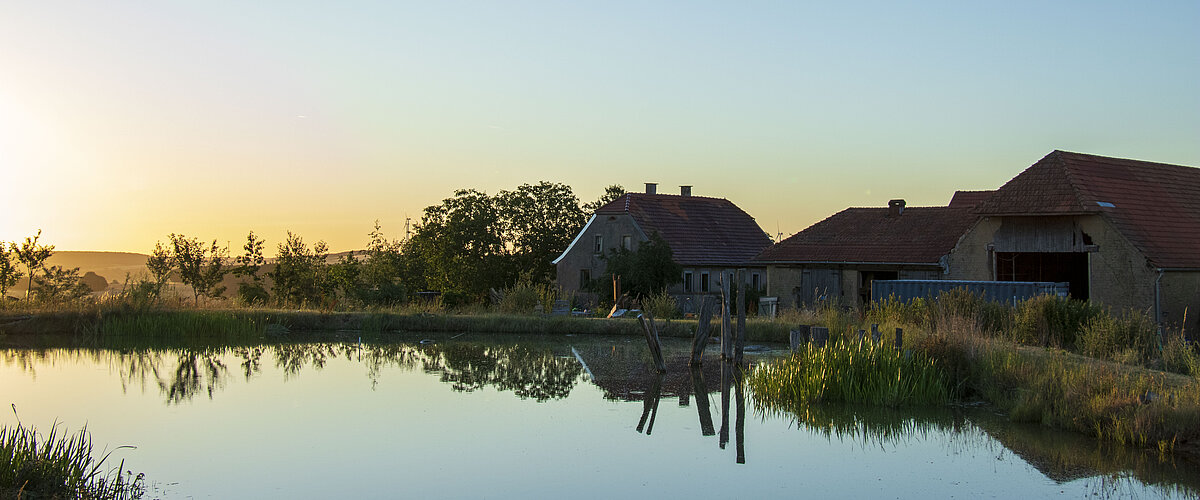 Humusland Hof Nordpfalz – Abenddämmerung Humusland Hof in der Nordpfalz – Hofgebäude spiegeln sich im Teich bei Abenddämmerung
